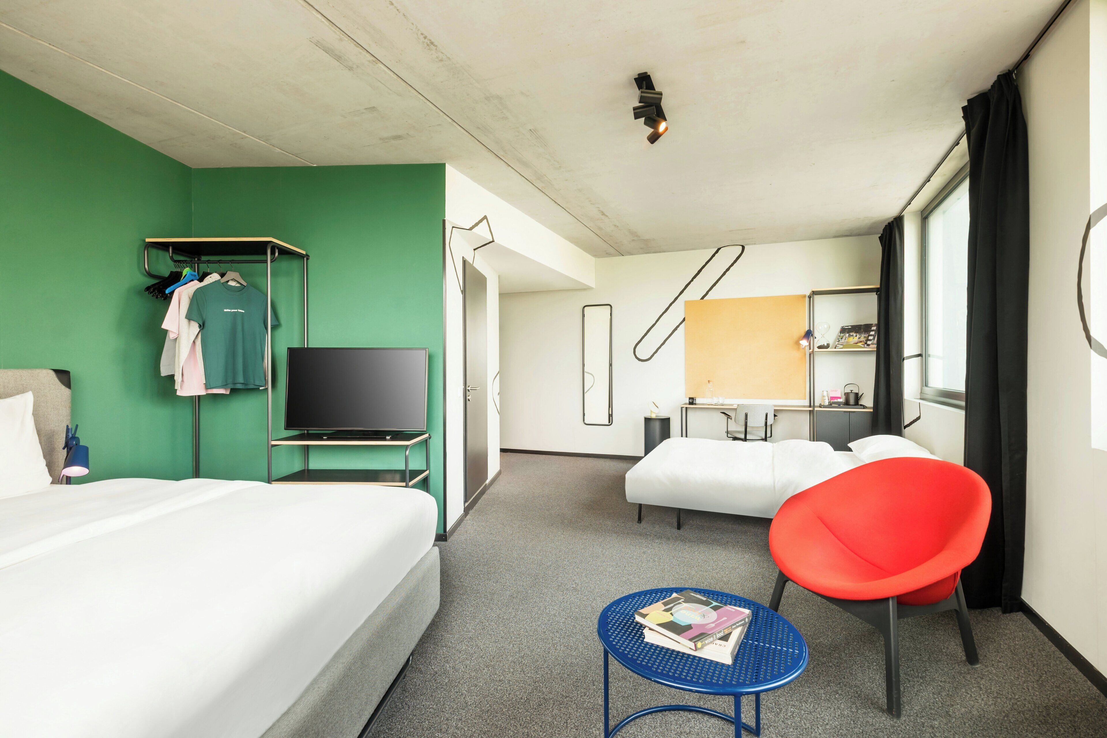 Ein Hotelzimmer mit Bett, Fernseher, rotem Sessel, kleinem Tisch und grüner Wand.