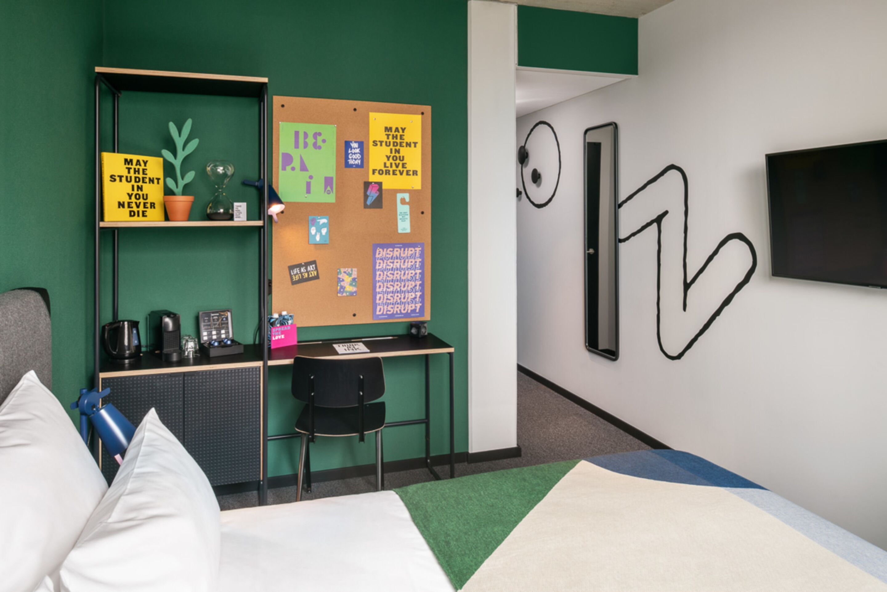 A modern room with a bed, a desk, a bulletin board, and a TV.