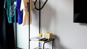 Habitación de hotel con dos camas, un perchero con ropa colgada, una mesita con una caja de pañuelos y el control remoto, y un televisor montado en la pared.