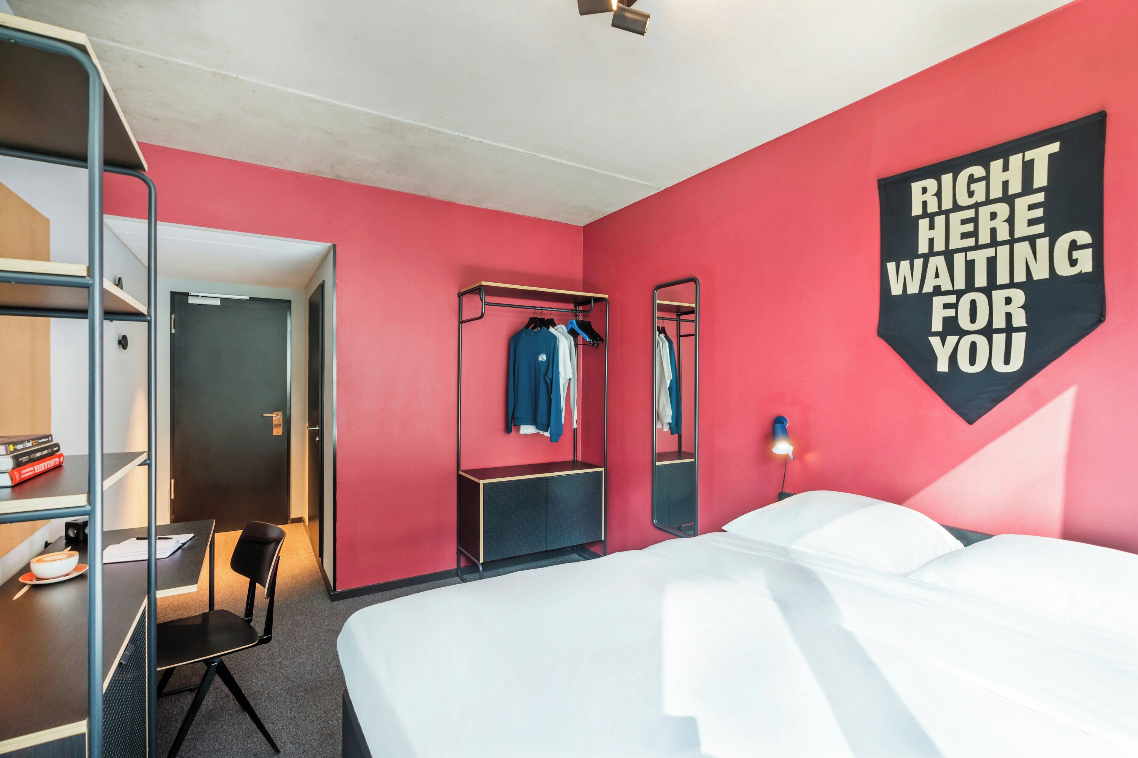 A hotel room with a bed, a desk, a chair, a wardrobe, and a mirror.