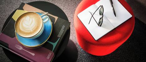 A table with a coffee cup, a book, and a red ottoman with sunglasses and a pen on it.