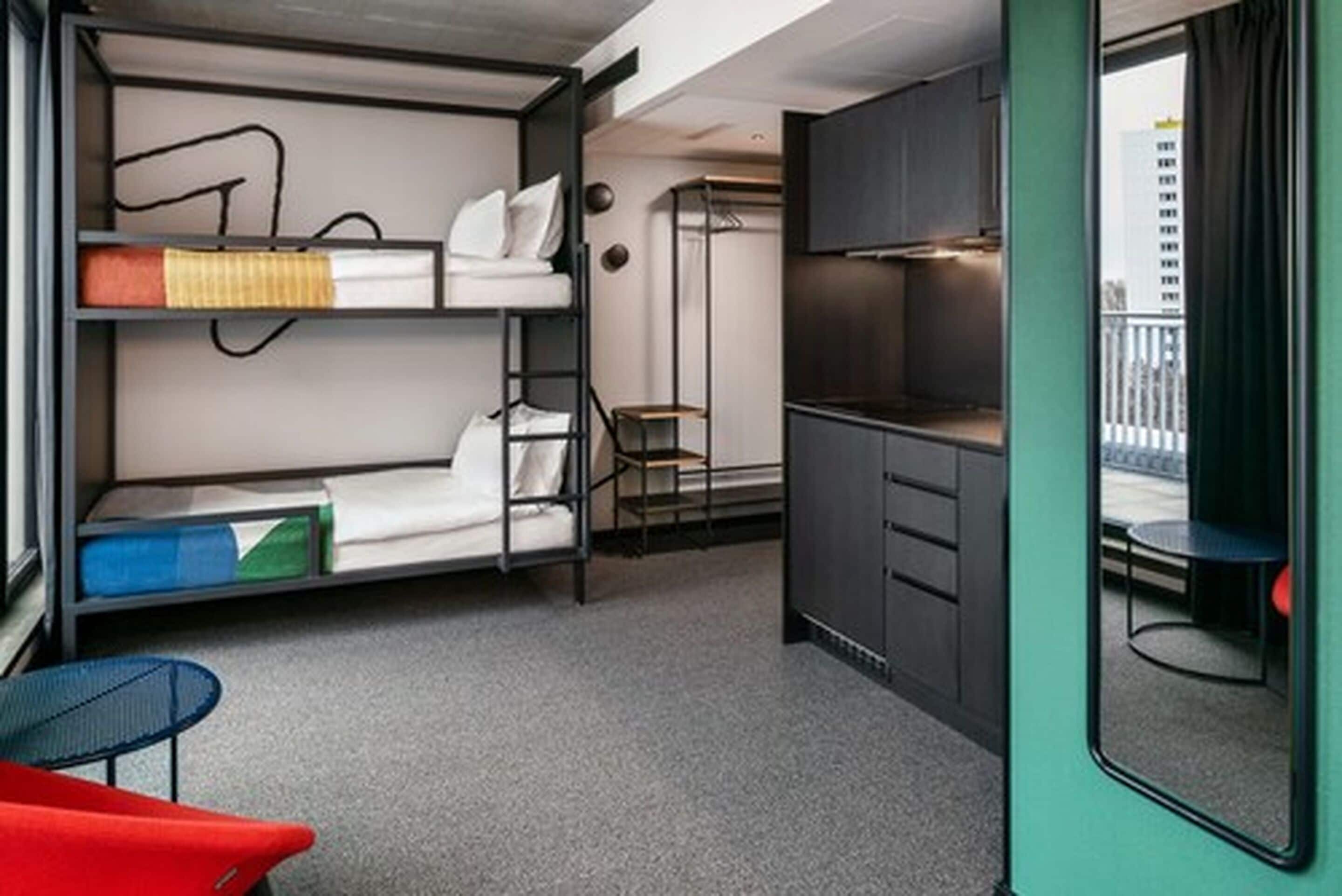 Een compacte hotelkamer met stapelbedden, een kitchenette, een klein tafeltje en uitzicht op de stad.