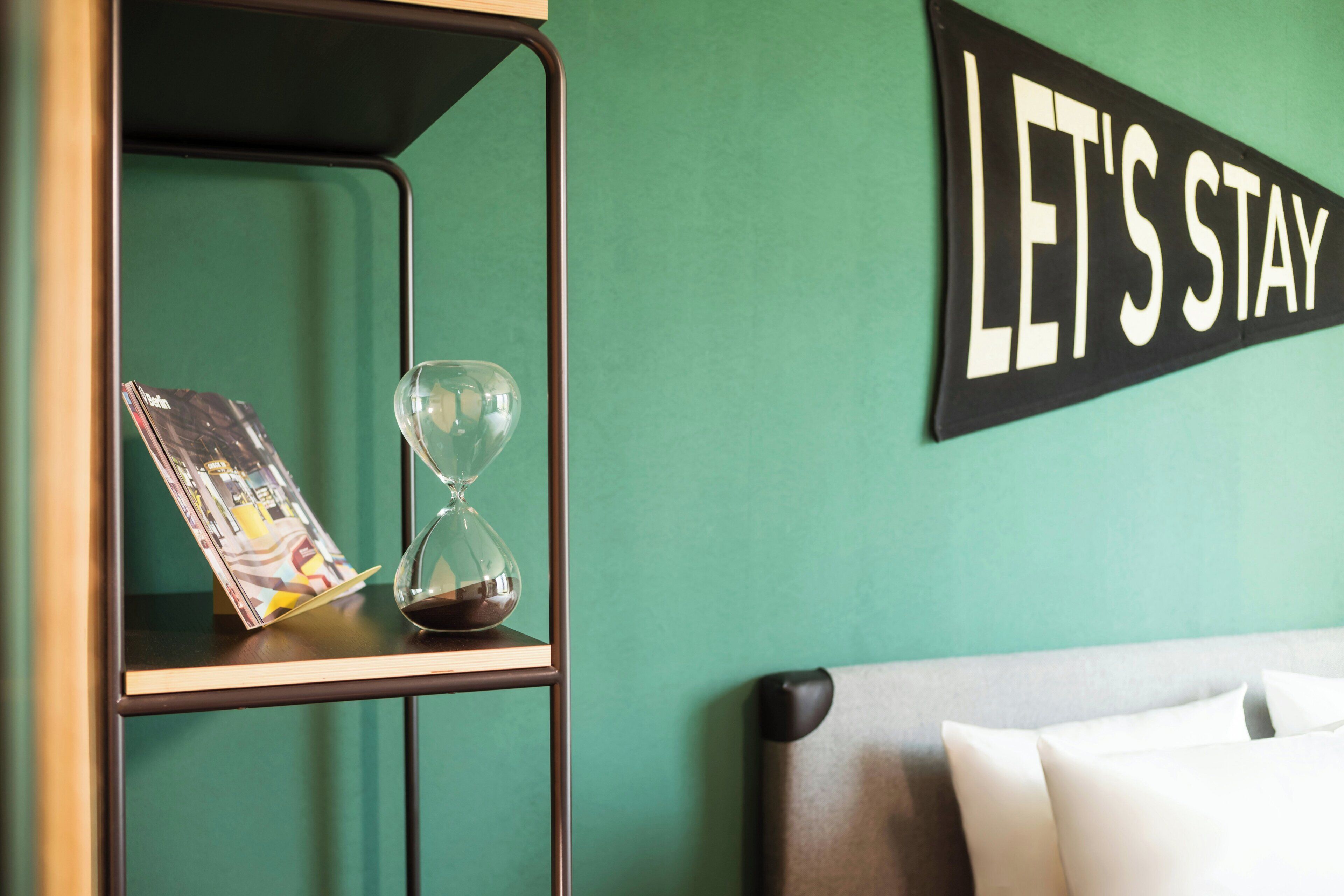 Une pièce avec un mur vert, une étagère avec un magazine et un sablier, et une pancarte sur laquelle on peut lire : « RESTONS ENSEMBLE ».