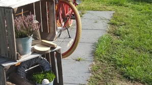 Un vélo est garé sur un trottoir, à côté d’une clôture en bois, et un panier rempli de fleurs est posé à proximité.
