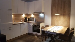 Una cocina compacta con gabinetes blancos, horno empotrado y una mesa de comedor con sillas.