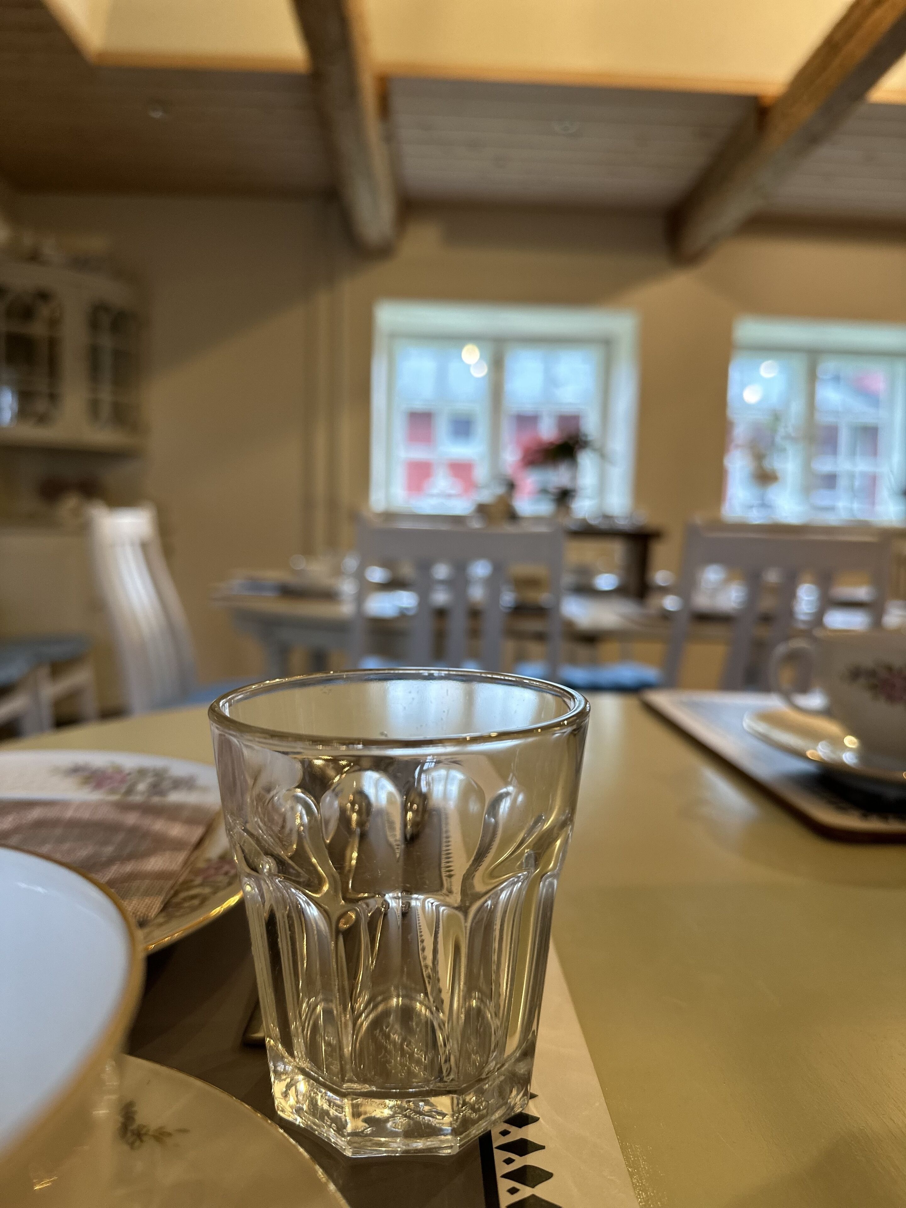 Et gennemsigtigt glas på et bord med en underlagsvægt, en hvid tallerken og en blomstret serviet.