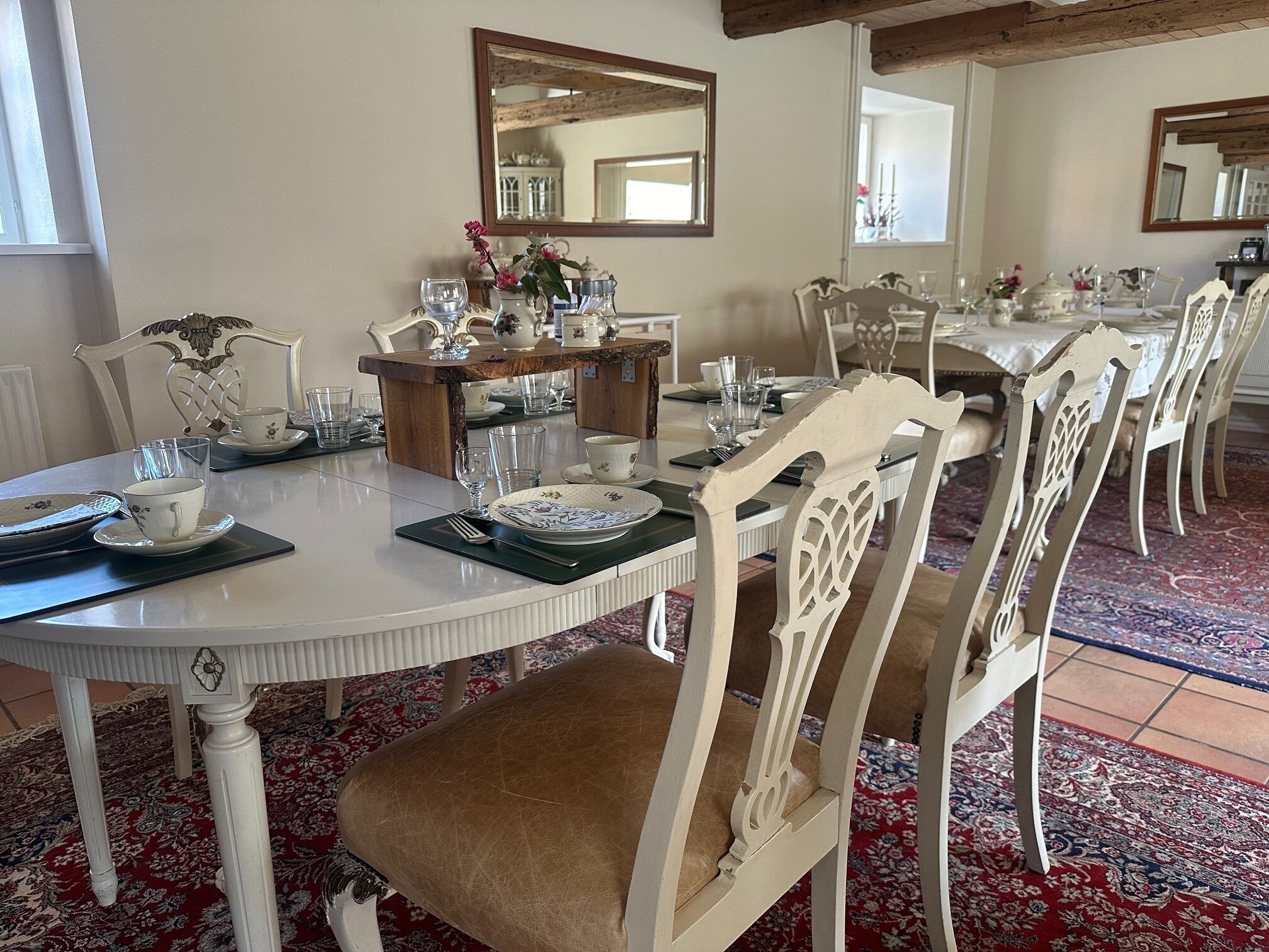 A dining area with white furniture, a wooden table, and a mirror on the wall.