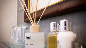 A bathroom shelf with a Nord fresh linen candle, two glass containers, and two bottles of liquid soap.