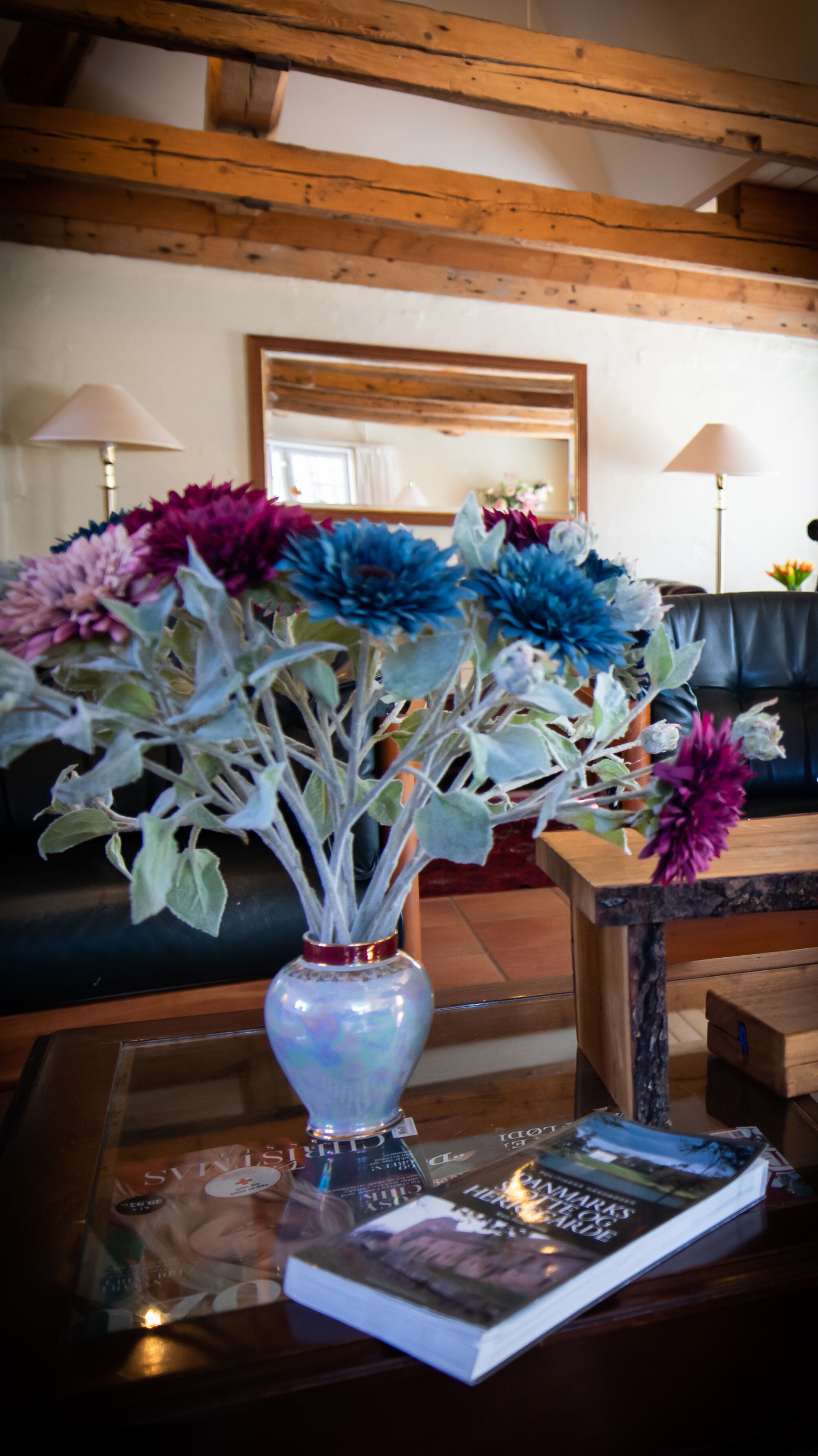 A room with a wooden ceiling, a sofa, a coffee table with a vase of flowers, and a magazine.