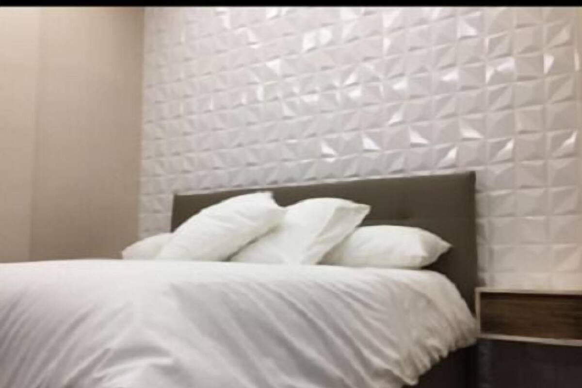 Ein ordentlich bezogenes Bett mit weißer Bettwäsche und Kissen, ein Kopfteil und eine strukturierte Wand dahinter.