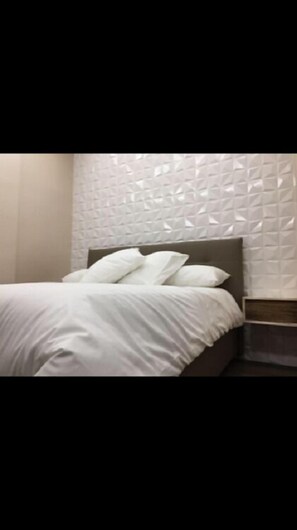 A neatly made bed with white bedding and pillows, a headboard, and a textured wall behind it. - B&B Il Duomo (Gioia Tauro)