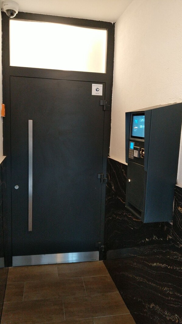 Una habitación de hotel con una puerta oscura, un ventanal pequeño y un panel de control con pantalla.