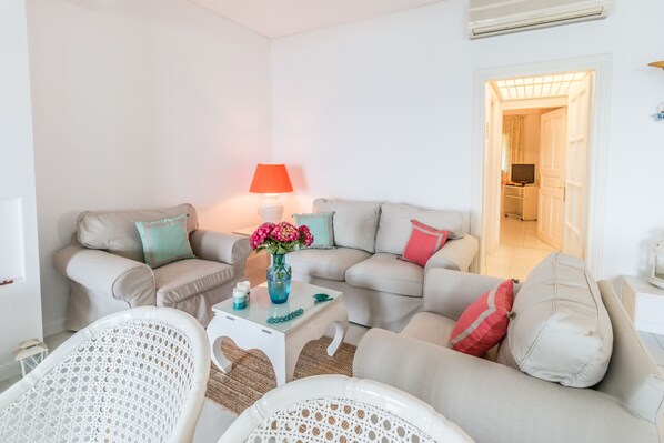 A living room with a beige sofa set, a white coffee table with a vase of flowers, and a red lamp. - Agios Ioannis Luxurious Beachfront Apt (Zagora-Mouresi)