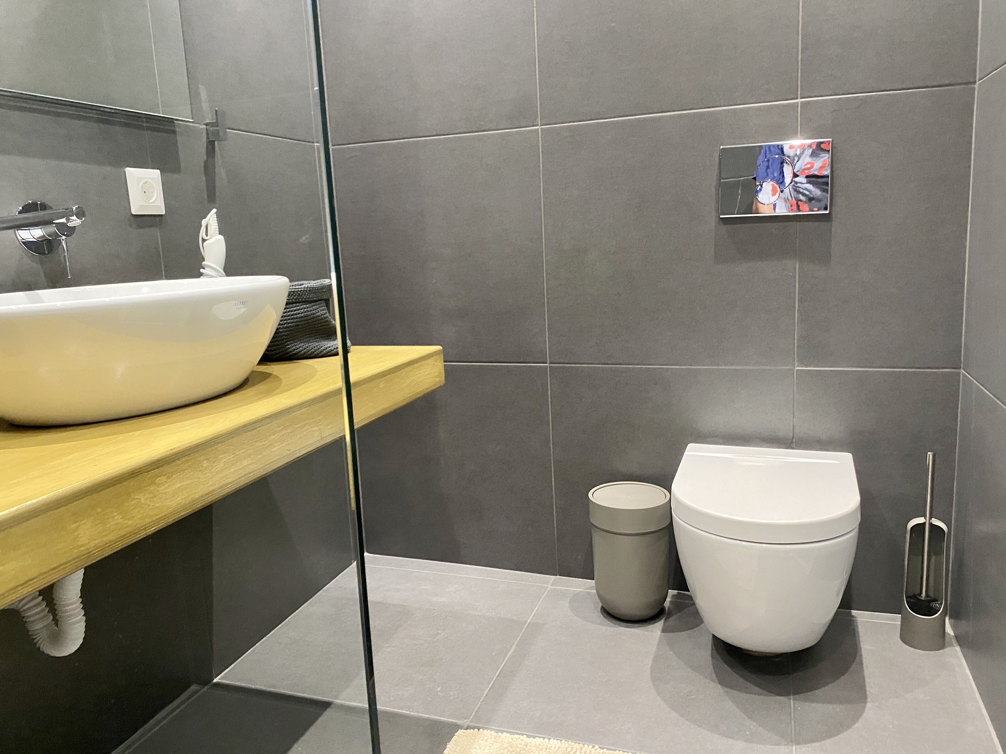 A modern bathroom with a large white sink, a toilet, and a trash bin.
