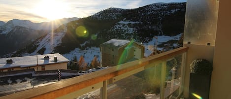 A balcony with a view of a snow-covered mountain and a small building.