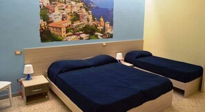 Habitación con dos camas, una mesita de noche con lámpara y un cuadro en la pared de un pueblo costero.