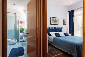 A bedroom with a bed, a bedside table, a window with curtains, a shower area, and a bathroom with a toilet and sink. - Welcome to Loretta's (Lido di Ostia)
