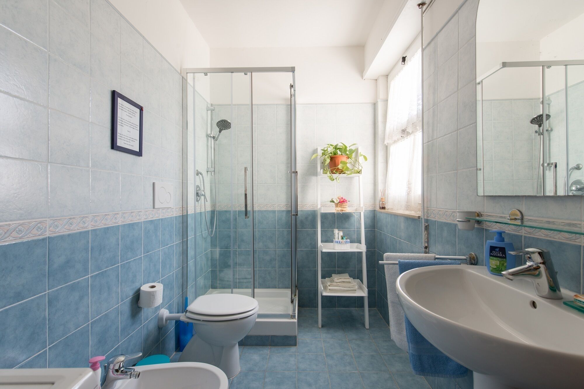 Een badkamer met een douche, toilet, wastafel en een glazen plank met toiletartikelen.