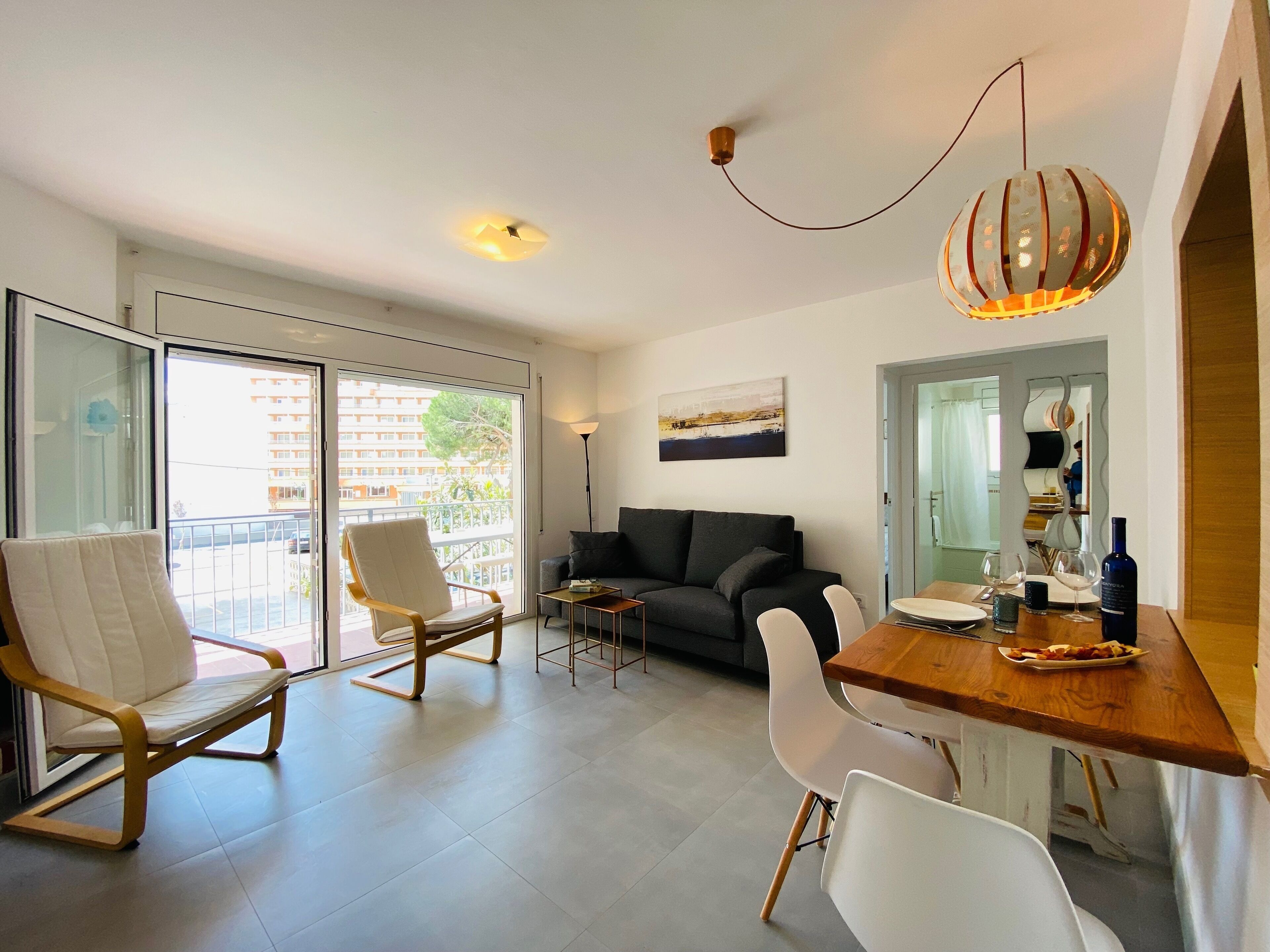 Ein modernes Wohnzimmer mit einer Couch, Sesseln, einem Esstisch und einem Balkon mit Glastüren.