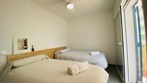 Habitación de hotel con dos camas, ventilador de techo, ventana con vistas y una obra de arte en la pared.