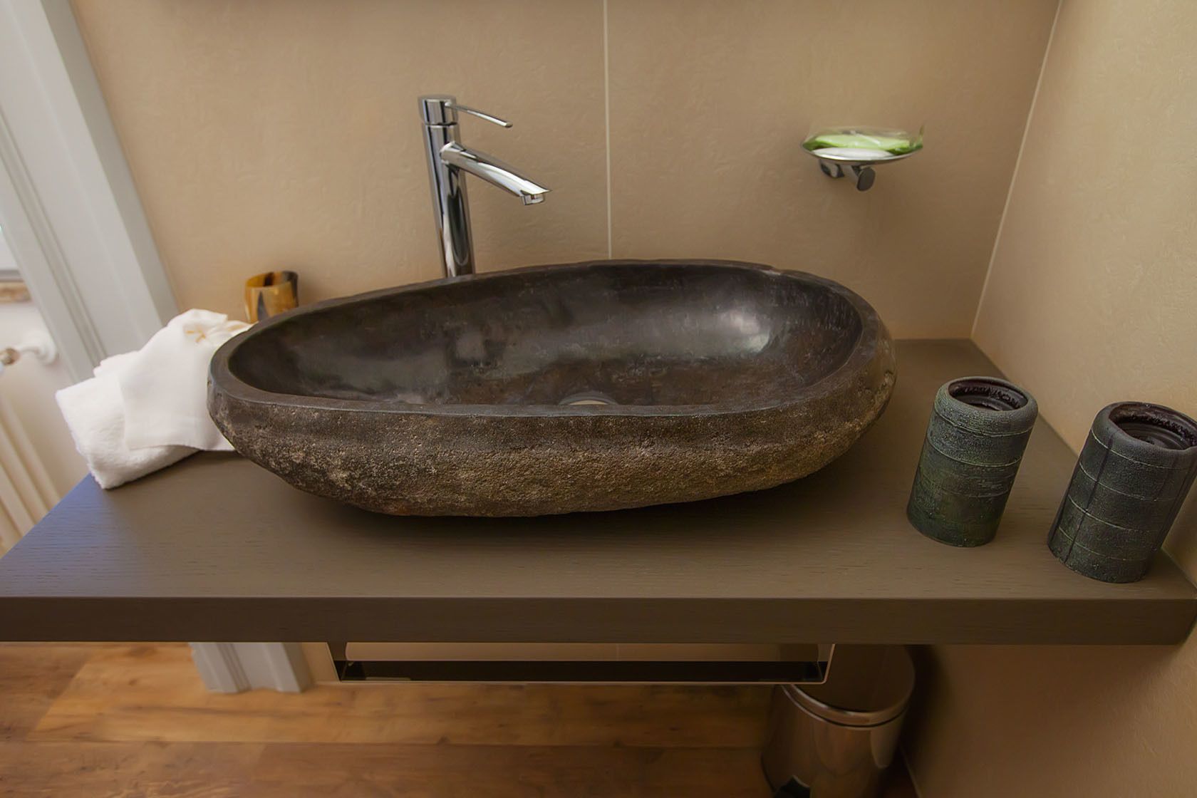 Een badkamer met een stenen wastafel, een moderne kraan en een klein plankje met toiletartikelen.