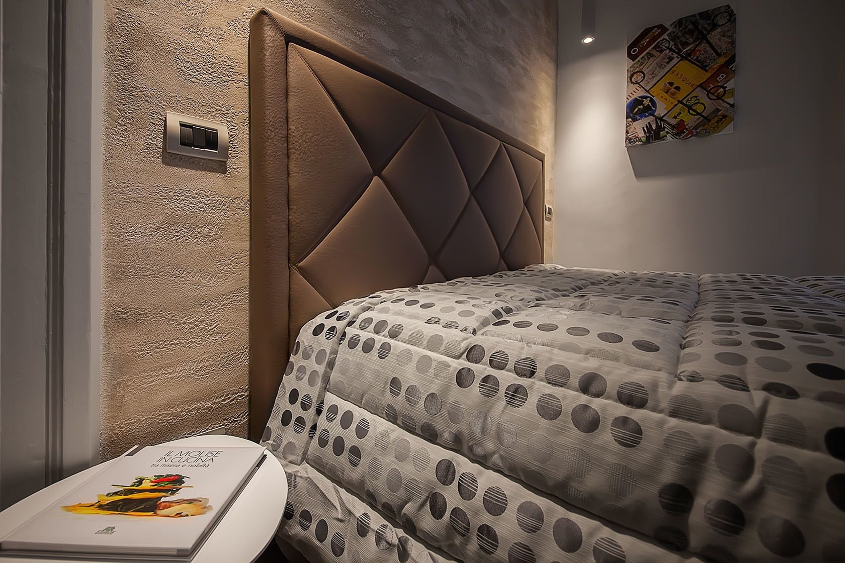 A bedroom with a tufted headboard, a polka dot bedspread, and a framed picture on the wall.