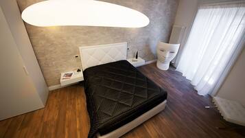 Um quarto moderno com uma cama, uma mesa de cabeceira, uma luminária grande fixada na parede, um radiador e uma janela com cortinas.