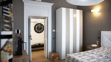 Un dormitorio con cama, mesita de noche, cómoda, un reloj de pared y una puerta que da a otra habitación.
