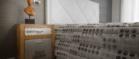 A bedroom with a bed, a nightstand with a vintage suitcase, and a wall-mounted light switch.