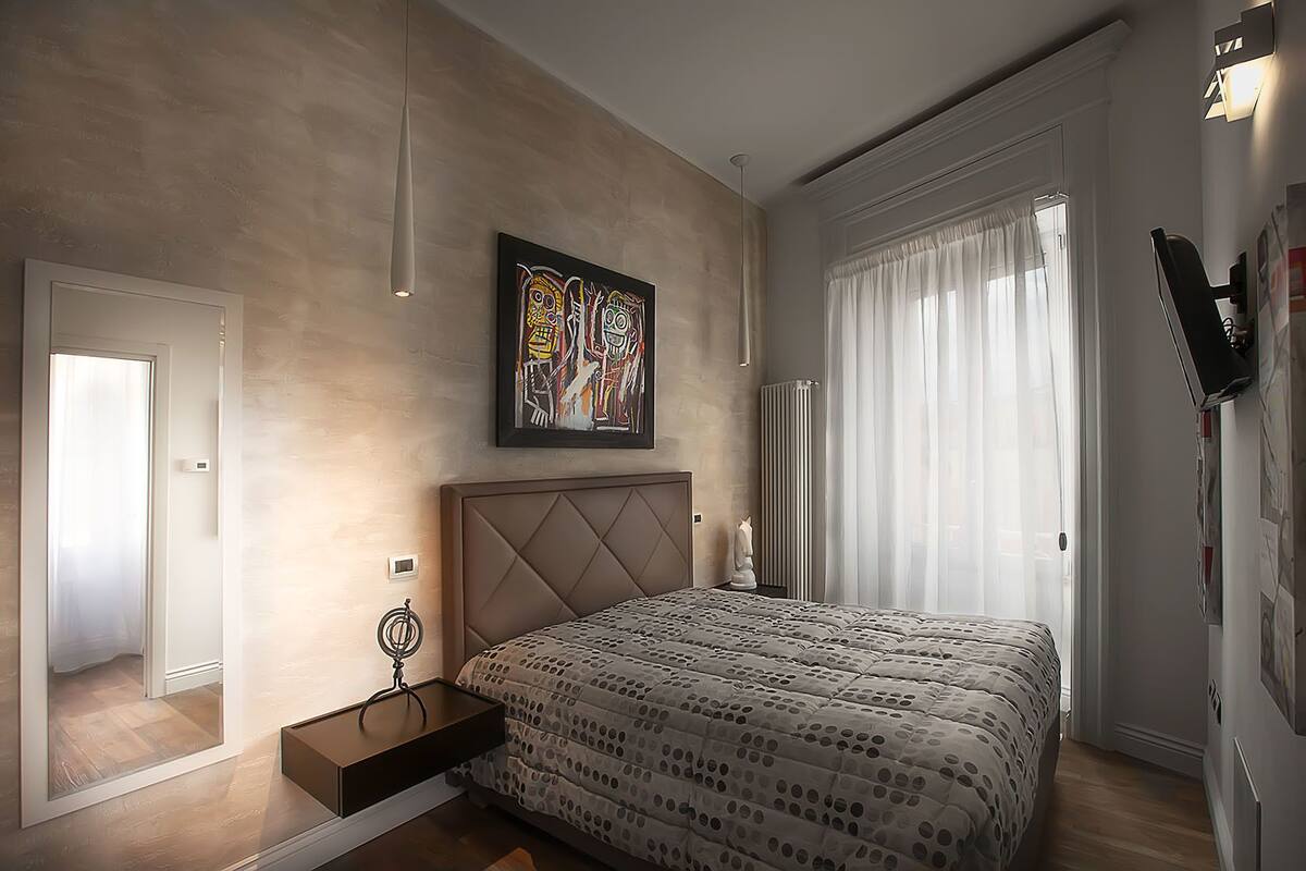 A modern bedroom with a large bed, a bedside table, a radiator, and a window with curtains.