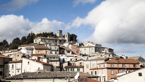 Un pueblo histórico con edificios de tejas de arcilla, una iglesia destacada con un campanario y un castillo al fondo.