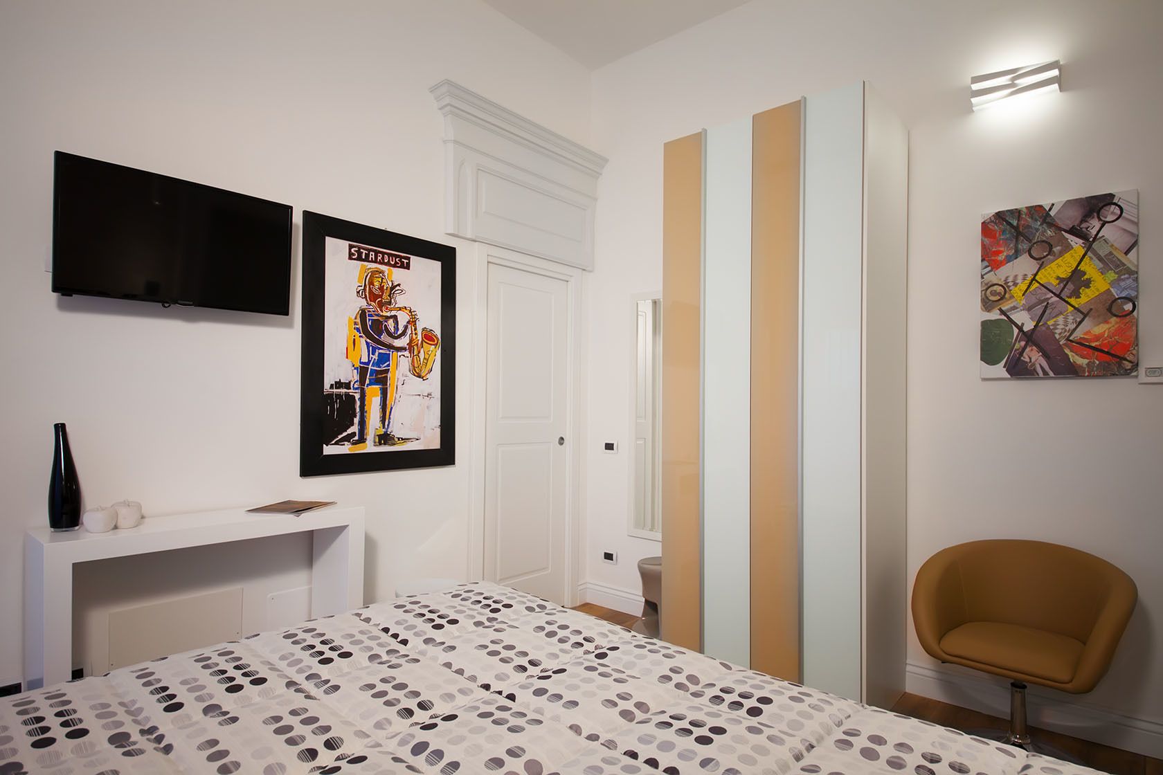 A bedroom with a bed, a TV, a framed poster, a chair, and a door.