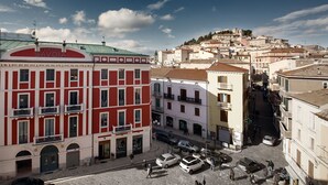 Vista de una calle con un edificio rojo que tiene la leyenda "Teatro Savoia" y un edificio blanco con el letrero "Manuel Zed".