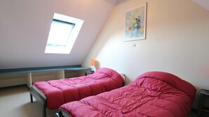 Un petit studio avec deux lits, une lucarne et un tableau accroché au mur.