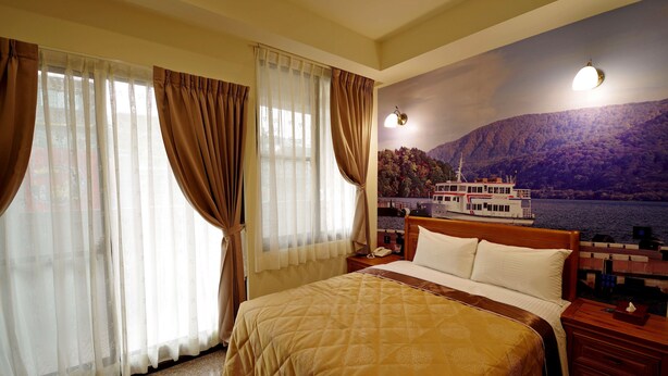 Une chambre d’hôtel avec un grand lit, une table de chevet, une lampe et une fresque murale représentant un bateau sur l’eau.