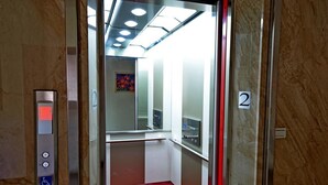 Un ascenseur doté d’un tapis rouge, d’un panneau de commande affichant le symbole d’accessibilité pour les personnes en fauteuil roulant, et d’un panneau indiquant le numéro 2 sur le mur.