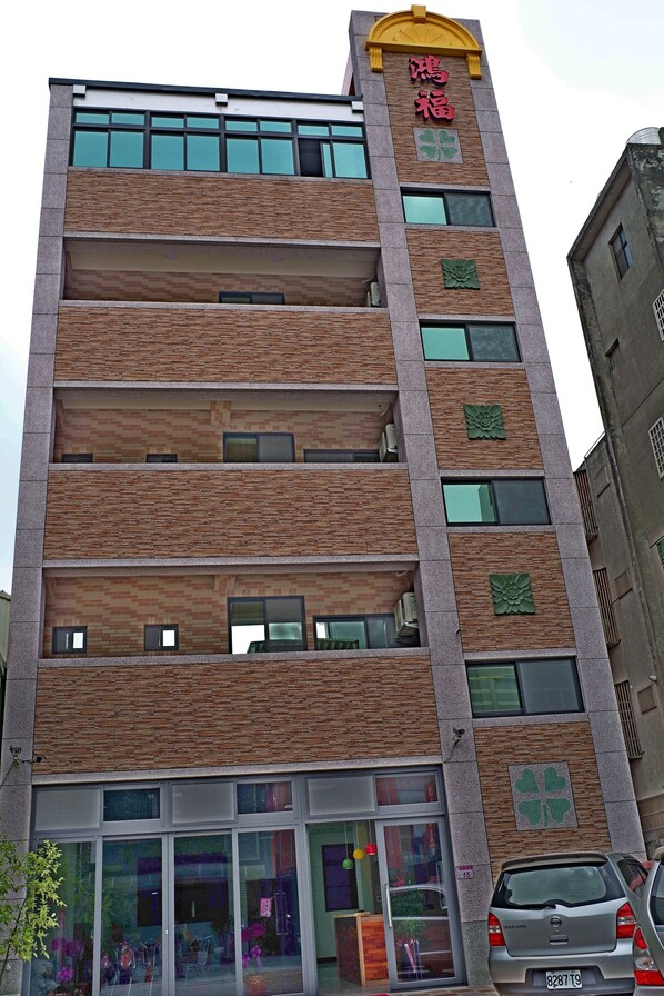 A multi-story building with a modern design, featuring a prominent entrance with glass doors and a visible car parked in front.