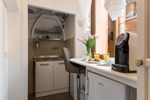 A compact kitchenette with a coffee maker, a small fridge, and a window with curtains. - Domus De' Fiori (Rome)