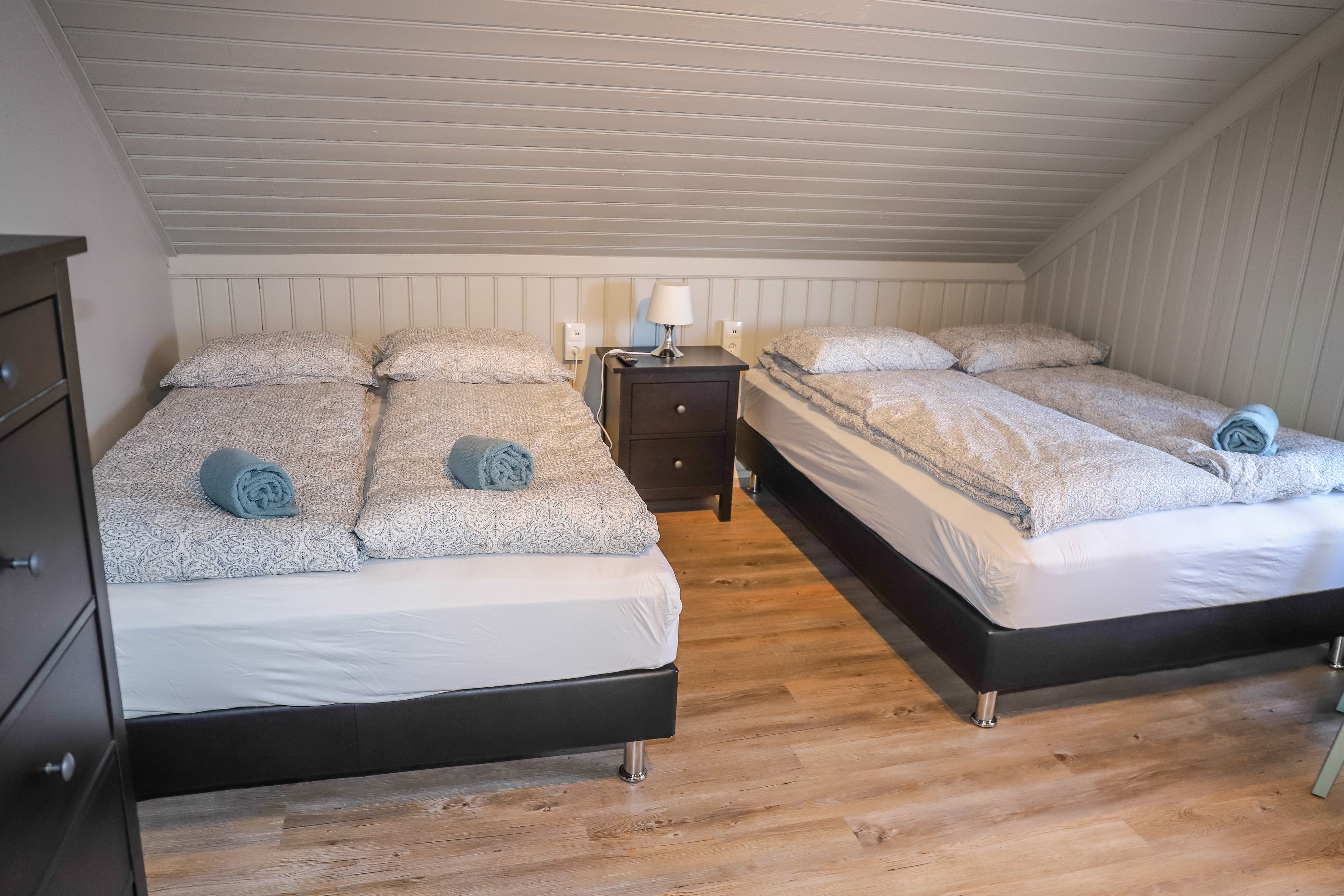 A room with two beds, a nightstand with a lamp, and a dresser.