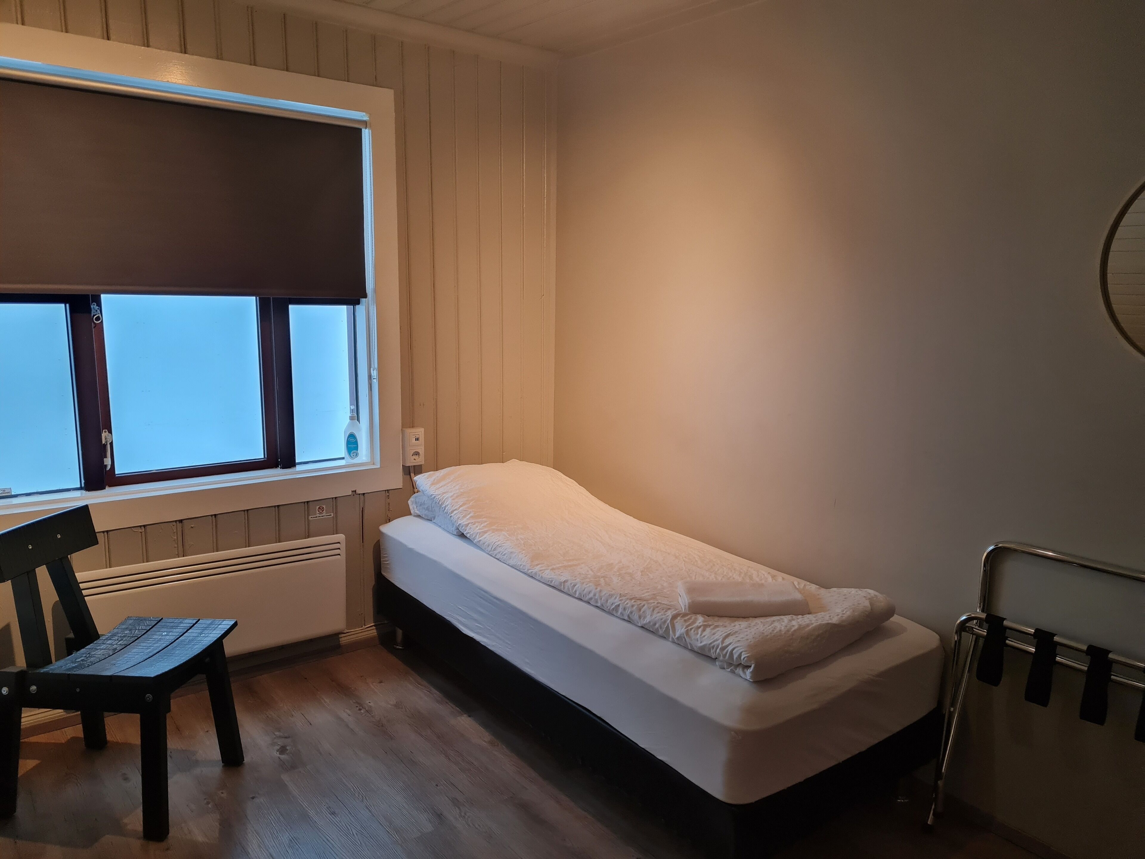 Habitación pequeña con cama individual, ventana, silla y radiador.