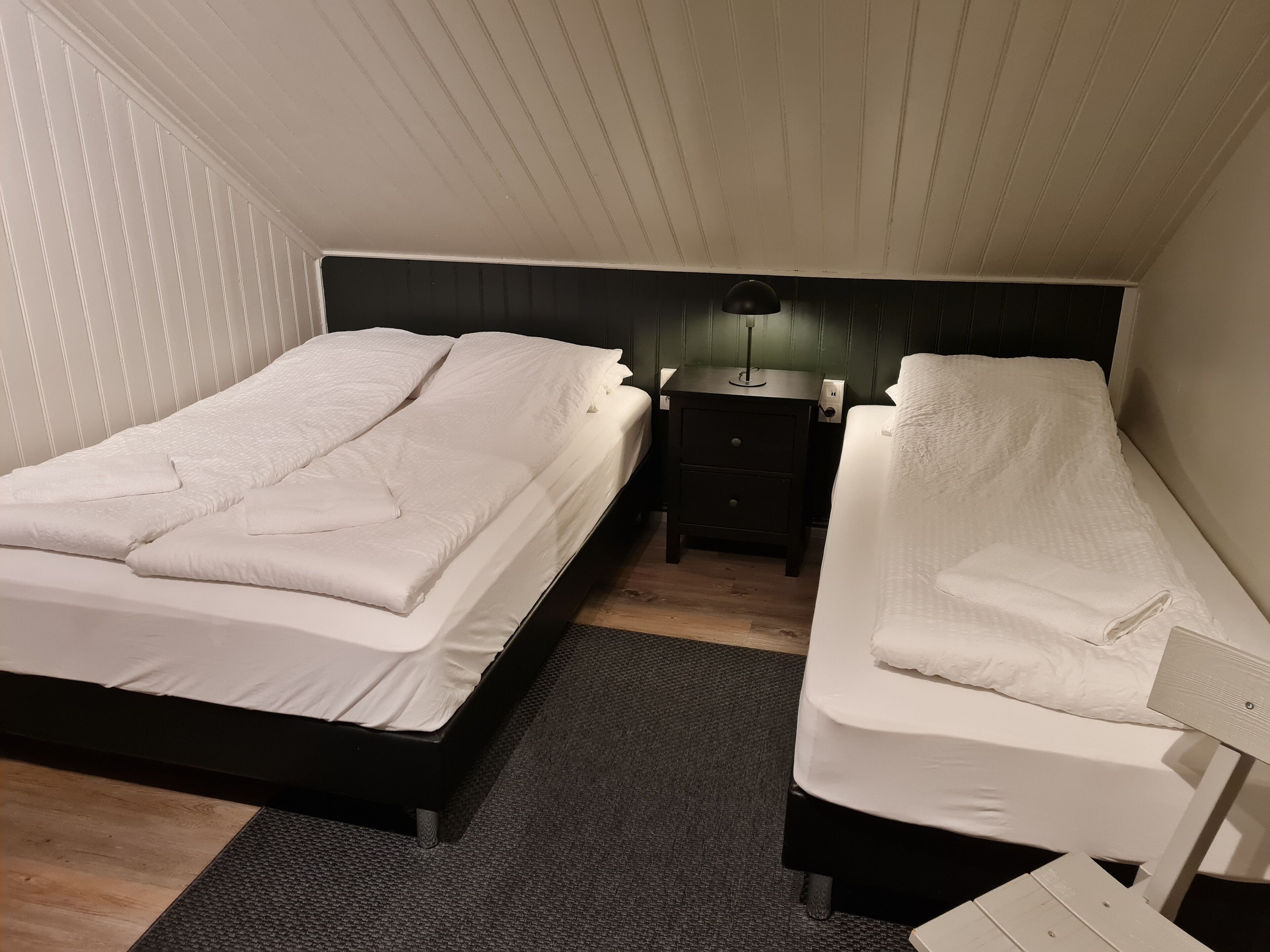 Quarto com duas camas, uma mesa de cabeceira e uma luminária.