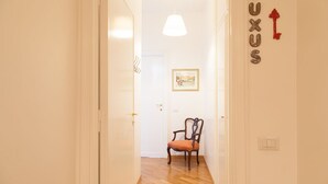 A hallway with a wooden floor, a chair, a door, and a wall with the word "LUXUS" and a red key decoration. - Cicerone 60 (Rome)