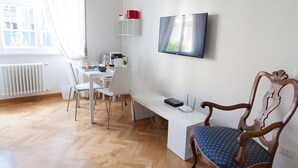 A modern living room with a wooden floor, a white desk, a television, and a wooden chair. - Cicerone 60 (Rome)