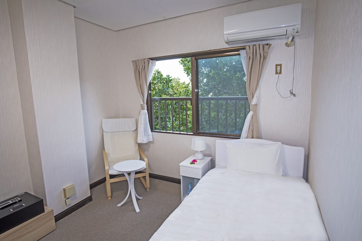 A hotel room with a bed, a small table, a chair, and a window with curtains.