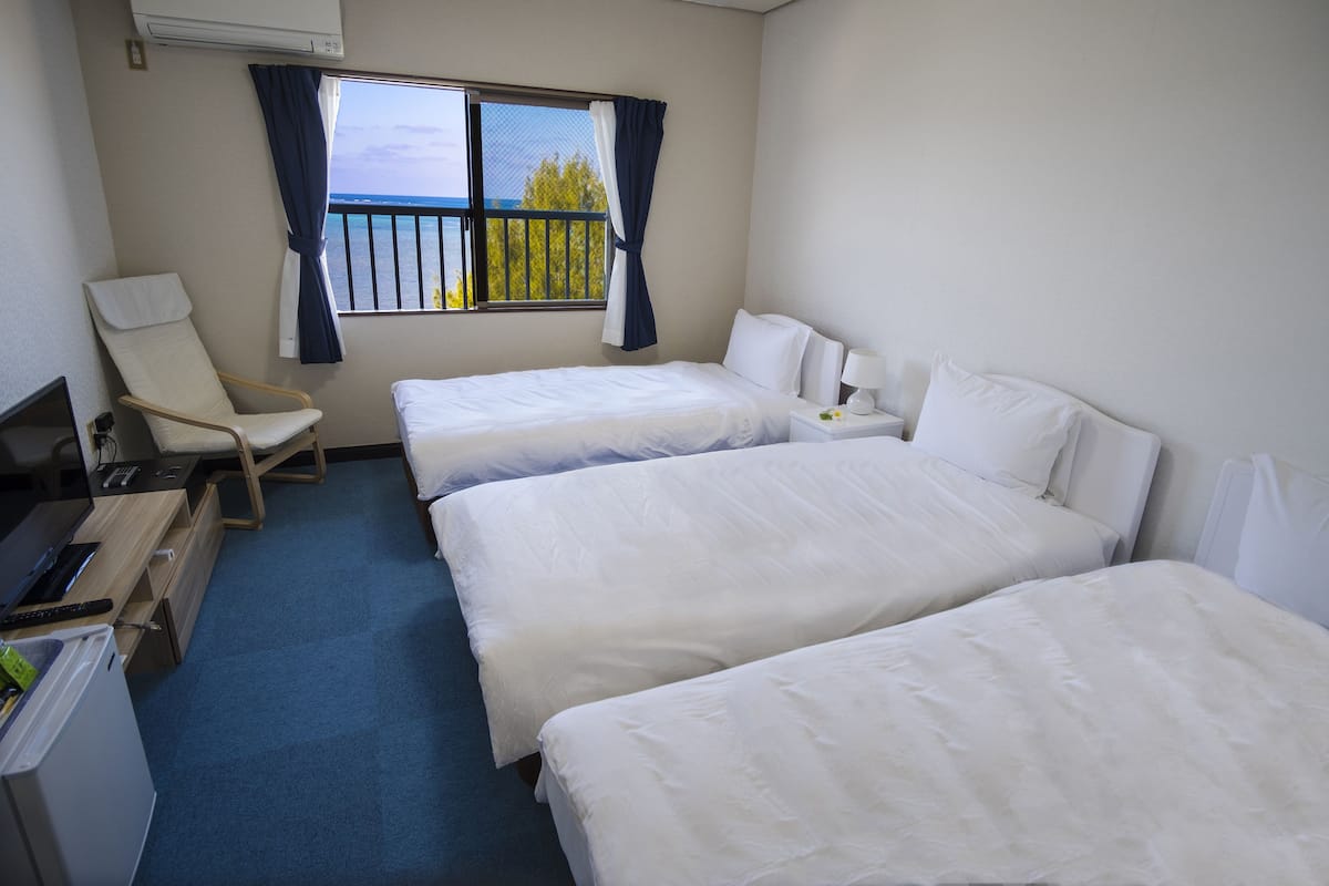 A hotel room with two beds, a desk with a computer, a chair, and a window with curtains.