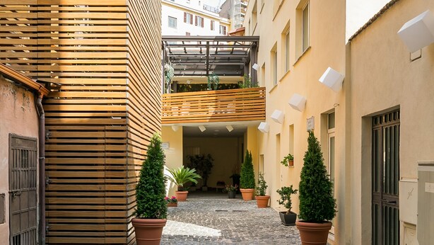 A cobblestone alleyway with buildings on either side, a wooden slatted wall, and potted plants. - Borghetto Guest House (Rome)