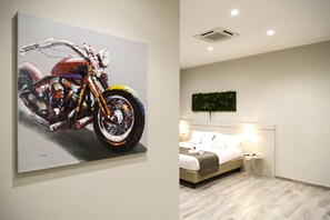 A room with a bed, bedside table, and a painting of a motorcycle. - Borghetto Guest House (Rome)