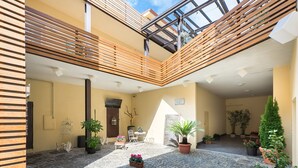 A spacious courtyard with a tiled floor, wooden slatted balconies, potted plants, and a seating area with a table and chairs. - Borghetto Guest House (Rome)