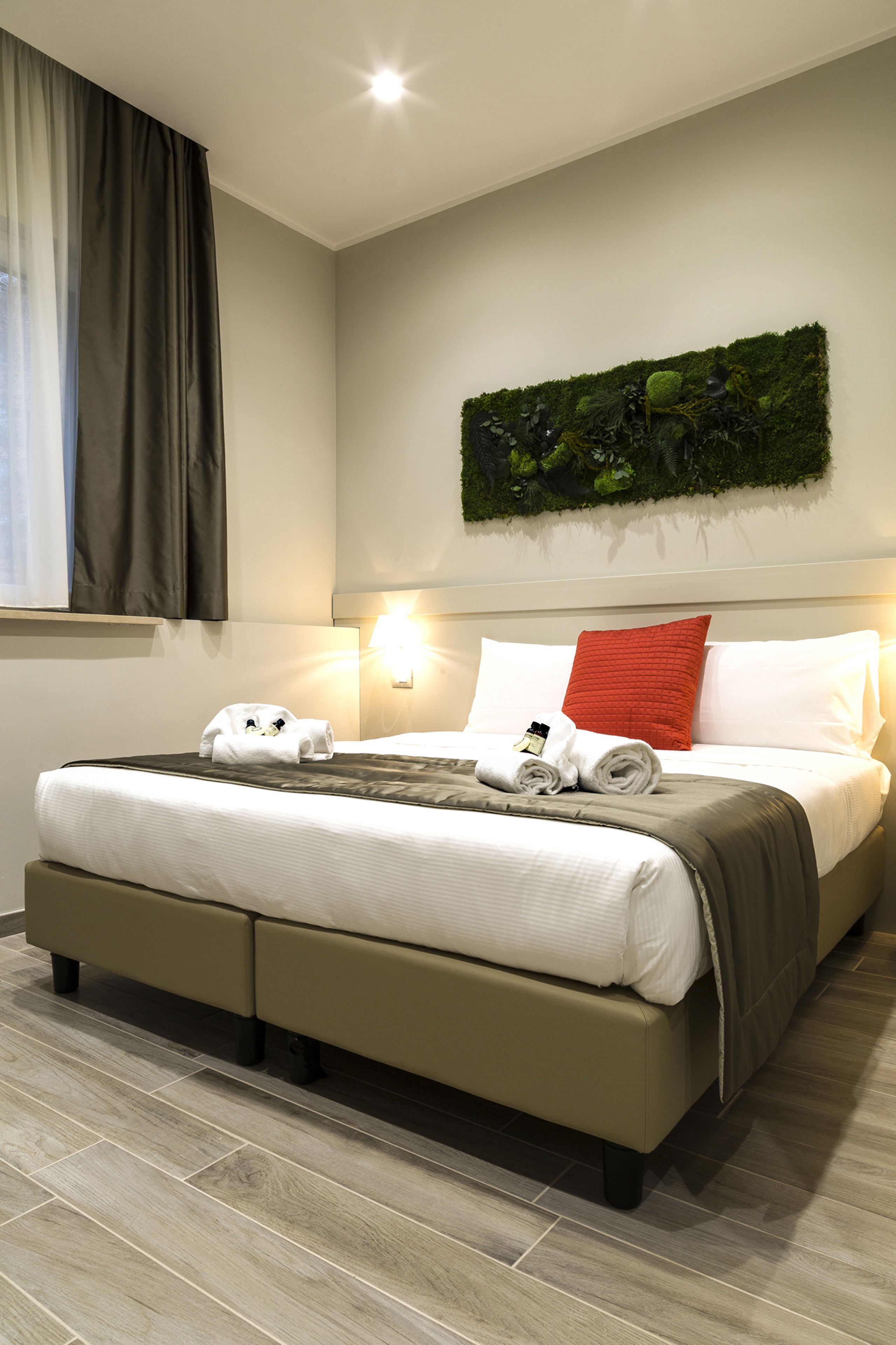 A neatly made bed with white linens, a red pillow, and a green wall art piece above it.