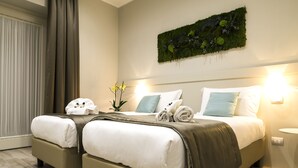 A hotel room with two beds, a green wall decoration, and a bedside table with a lamp. - Borghetto Guest House (Rome)